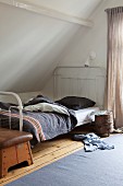 Tree stump table on castors and clothing on floor next to metal-framed bed with grey cover; old vaulting horse at foot of bed