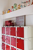 Spielzeugauto auf ausrangiertem Schließfachschrank mit rot lackierten Türen; darüber auf einem Balken eine Sammlung Quietschfiguren