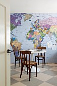 Old, bentwood chairs and office utensils on white Tulip table in front of wallpaper mural showing map of the world