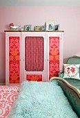 Old wardrobe with panels decorated with floral wallpaper and curtains; antique bed with turquoise faux fur blanket