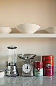 White china bowls on floating shelf and colourful Chinese tea caddies next to retro kitchen appliances on marble counter