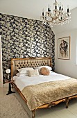 Double bed with gilt, antique wooden frame against wall with black and white floral wallpaper