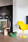 Gelber Schalenstuhl von Eero Saarinen und Stuhl in Form einer aufgestellten Hand vor Buddha-Bild