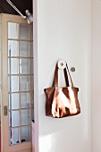 Brown leather bag hanging on peg next to lattice door