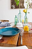Blauer Teller und Glasvasen mit Blumen auf Holztisch
