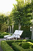 Two deckchairs amongst topiary box hedges in garden surrounded by espalier trees and tall hedges