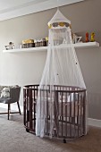 Oval cot with canopy, storage baskets on white shelf on pale grey wall