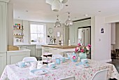 Breakfast table set with pale blue crockery in front of open-plan, country-house kitchen