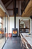 Rustic dining area below modern gallery in open-plan, renovated country house with fire in wood-burning stove