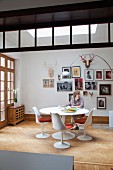 Woman sitting on Tulip chair at matching table in front of framed photos on white wall