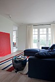 Blue sofa and drum-shaped side table on striped rug opposite red artwork leaning against wall