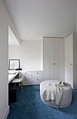 Pale ottoman on blue carpet, white fitted wardrobe and workspace with classic chair