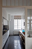 Blick in zweizeilige Küche mit Einbaumöbeln und Sideboard; Trennwand mit Sprossenfenstern im Vordergrund
