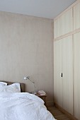 Puristisches Schlafzimmer mit weiss bezogenem Bett und schlichtem Einbauschrank aus hellem Holz