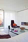 Designermöbel und Feuerstelle in weißer Wandscheibe, bodenlanger Vorhang vor Verglasung in elegantem Wohnzimmer
