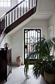 Staircase with turned wooden balusters in foyer with potted palms in front of glass front door