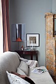 Hellgraue Couch mit Kissen in Wohnzimmerecke, im Hintergrund antiker, halbkreisförmiger Wandtisch an grau getönter Wand