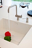 White sink in designer Corian kitchen worksurface; water running onto bell peppers