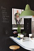 Pendant lamp with green metal lampshade above breakfast bar against wall painted with black chalkboard paint