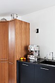 Schwarzer Küchenunterschrank mit Espressomaschine, daneben Holzschrank