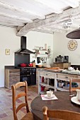 Mediterranean kitchen with rustic wood-beamed ceiling - view across dining table to free-standing counter