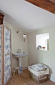 Bathroom with white and blue-painted pedestal sink and laundry basket below small window