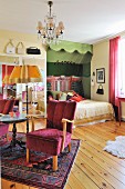 Feminine bedroom; retro armchair with red cover next to side table and standard lamp and double bed in niche decorated in shades of green