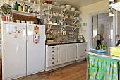 Kitchen counter with white base units, crockery on wall-mounted bracket shelves and fridge-freezer combination in simple country-house kitchen