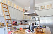 Scandinavian fitted kitchen - extractor hood above island counter with fitted cooker and wooden ladder leading to illuminated wall cabinets