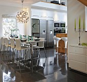 Set dining table in front of open-plan, fitted kitchen with stainless steel appliances and designer bar stools at island counter