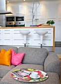 Grey sofa with colourful scatter cushions in front of bar stools at kitchen island