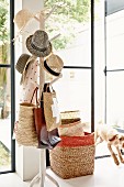 Collection of hats on tree-like coat stand, stacked baskets and open terrace door with view into garden