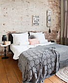 Grey crocheted bedspread on double bed against partially plastered brick wall in bedroom with wooden floor