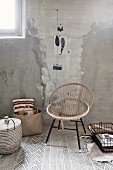 Shell chair made from curved rattan on black metal frame next to bag and basket on patterned rug in industrial, unrenovated interior