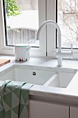 Marble worksurface with integrated sink and white tap fittings below window with a view