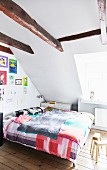 Bedroom with exposed ceiling beams, colourful children's drawings on wall and plain wooden floor