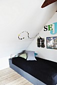 Single bed under sloping ceiling with creative arrangement of ornaments and decorative lettering on walls