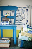 Vogelfigur und Box mit Blumenmuster auf blau lackiertem Holzstuhl, seitlich Handtuchstapel