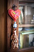 Key pendant with heart-shaped cushions and ribbon tassel hanging from key of glass-fronted cabinet