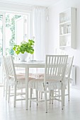 White dining room with frilled cushions on wooden chairs and crockery shelves on wall