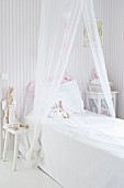 Bed with draped mosquito net and bunny soft toys leaning against pillow in child's bedroom