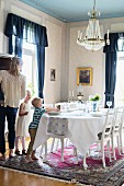 Mother and children in traditional dining room with festively set table below chandelier
