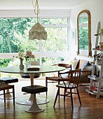 Tulip table, matching stools and wooden chairs in contemporary interior with view of garden