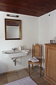 Sink below gilt-framed mirror next to antique chair in renovated bathroom