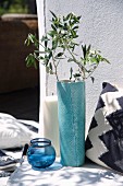Olive branch in turquoise vase, glass tealight holders, large pillar candle and cushion