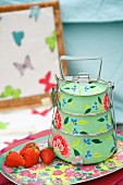Vintage-style dinner pail with floral pattern and fresh strawberries on tray