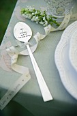 Ornamental spoon decorated with bow and sprig of white flowers on table