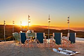 Luxuriöses Picknick am Strand mit Regiestühlen und kleinen Laternen an Stangen im Sand bei Sonnenuntergang