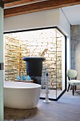 Free-standing designer bathtub and view of large planter in light well with stone wall