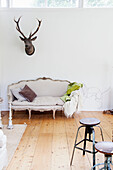 Antique couch with reindeer head on wall above in bright living room